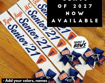 Può includere: Striscioni per anziani bianchi e blu navy con nomi e 'Senior 21' stampati. I nastri hanno accenti arancioni e bianchi, insieme a fiocchi blu navy. L'immagine include anche il testo 'Class of 2027 Now Available'.