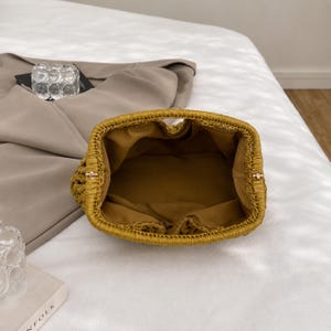 May include: A woven, mustard-yellow handbag with a rounded shape. The interior is lined with a matching fabric. The bag has a structured design and a small handle. The bag is open, revealing the interior.