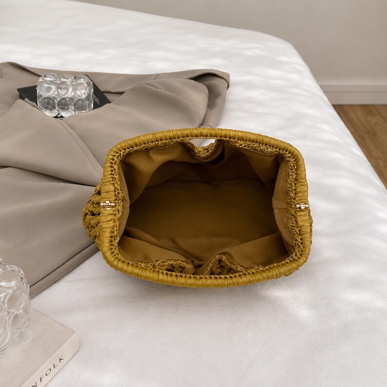 May include: A woven, mustard-yellow handbag with a rounded shape. The interior is lined with a matching fabric. The bag has a structured design and a small handle. The bag is open, revealing the interior.
