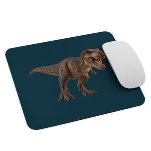 May include: A rectangular dark blue mouse mat featuring a brown Tyrannosaurus rex dinosaur with its mouth open, positioned centrally. A smooth white computer mouse rests on the right side of the mouse mat, partially overlapping the dinosaur graphic.