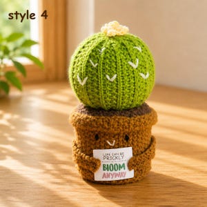 Peut inclure: Un cactus au crochet dans un pot marron avec une petite fleur jaune au sommet. Le pot a deux petits bras tenant un panneau rectangulaire blanc avec l'inscription : LIFE CAN BE PRICKLY BLOOM ANYWAY. Le cactus est vert vif avec des détails en V.