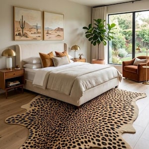 Peut inclure: Une chambre avec un lit beige rembourré, du linge de lit blanc, des coussins marron, un grand tapis à motif léopard, deux tables de chevet en bois avec des lampes dorées, un fauteuil marron et deux tableaux sur le thème du désert.