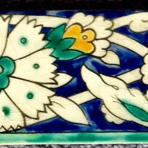 May include: A series of decorative ceramic tiles featuring a floral design. The tiles have a blue background with white, yellow, and green floral patterns. The design includes stylized flowers and leaves, with a green border at the bottom.