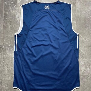 K&ouml;nnte beinhalten: Ein &auml;rmelloses, marineblaues Sporttrikot mit wei&szlig;en Zierleisten und Akzenten. Das Trikot hat einen Mesh-R&uuml;ckeneinsatz und das Adidas-Logo auf dem oberen R&uuml;cken. Es hat einen gebogenen Saum und einen Rundhalsausschnitt.
