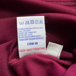 May include: Close-up of a burgundy fabric with a white tag. The tag displays washing instructions, including a maximum temperature of 40&deg;C/104&deg;F, and the text "KEEP AWAY FROM FIRE".