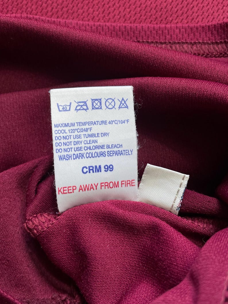 May include: Close-up of a burgundy fabric with a white tag. The tag displays washing instructions, including a maximum temperature of 40&deg;C/104&deg;F, and the text "KEEP AWAY FROM FIRE".