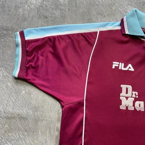 May include: Maroon Fila athletic jersey with light blue accents. The jersey features a white stripe, light blue collar and sleeve trim. The Fila logo is on the chest, and the words "Dr. Ma" are printed below.