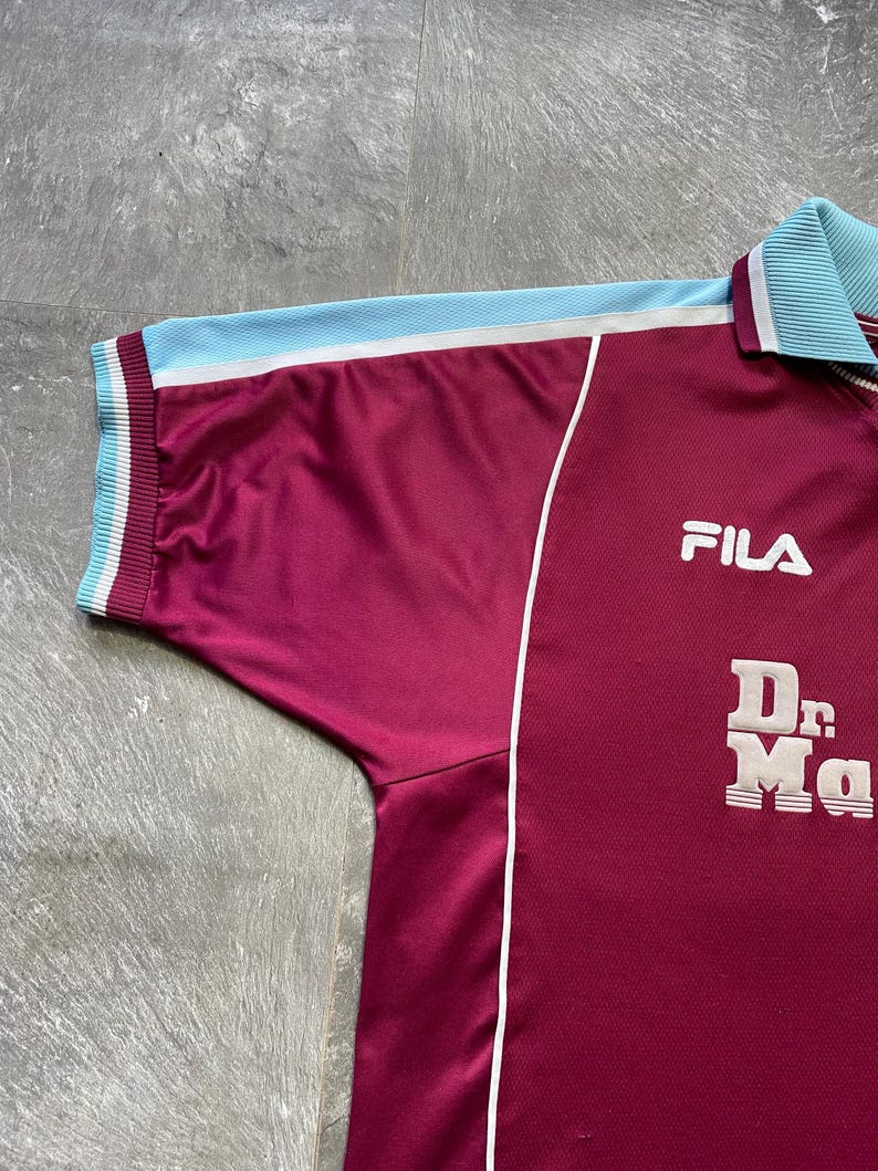 May include: Maroon Fila athletic jersey with light blue accents. The jersey features a white stripe, light blue collar and sleeve trim. The Fila logo is on the chest, and the words "Dr. Ma" are printed below.