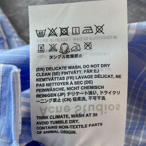 May include: A white rectangular garment care label with black text and laundry symbols. The label includes instructions for a delicate wash, avoiding tumble dry, and a note stating the item contains non-textile parts of animal origin.