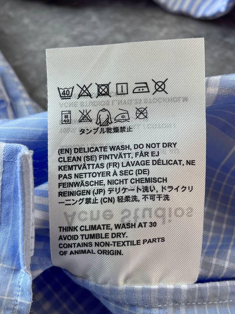 May include: A white rectangular garment care label with black text and laundry symbols. The label includes instructions for a delicate wash, avoiding tumble dry, and a note stating the item contains non-textile parts of animal origin.