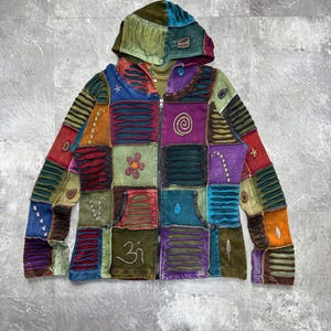 May include: A patchwork hoodie with a zip-up front. The jacket features a variety of colors and textures, including squares of blue, red, green, and purple. The hood is a mix of green and brown. The jacket has a front pocket and embroidered details.