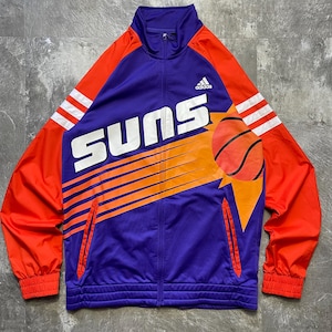 May include: A purple, orange, and white Adidas track jacket with the word "SUNS" across the front. The jacket features a basketball graphic and the Adidas logo. The sleeves are orange with white stripes.