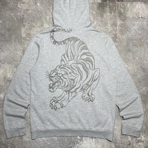 May include: A grey hooded sweatshirt featuring a large tiger design on the back. The tiger is illustrated in grey tones, with stripes and a snarling expression. The hoodie has a drawstring and ribbed cuffs.