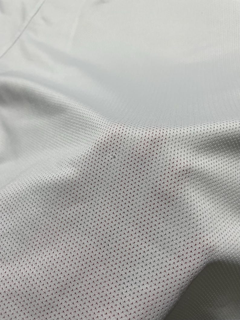 Puede incluir: Primer plano de una tela gris claro con un patr&oacute;n texturizado y perforado. La tela parece ser un material transpirable, posiblemente para ropa deportiva. La imagen resalta los finos detalles del tejido.