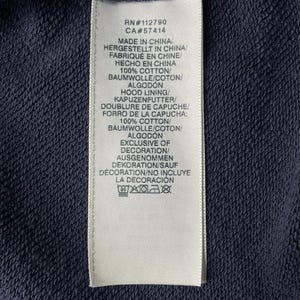 May include: Close-up of a navy blue fabric with a white tag attached. The tag includes text in multiple languages, including "MADE IN CHINA" and fabric composition details. The tag also lists RN and CA numbers.