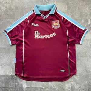 May include: Maroon football shirt with light blue collar and sleeve trim. The shirt displays the Fila logo, the Dr. Martens logo, and a team crest. White stripes run down the sides of the shirt.