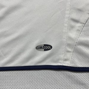 Puede incluir: Camiseta deportiva blanca con ribete azul marino y el logo "CLIMACOOL". La camiseta tiene un panel de malla en el lateral y una secci&oacute;n inferior perforada. La tela parece ser un material ligero y transpirable.