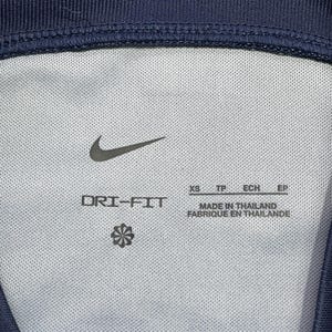 May include: A navy blue athletic garment interior featuring the text SAINT-GERMAIN, a black Nike swoosh logo, and the text DRI-FIT. The label indicates size XS, TP, ECH, EP and states MADE IN THAILAND, FABRIQUE EN THAILANDE with a small flower icon.