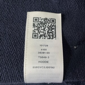 May include: Close-up of a navy blue fabric with a white tag attached. The tag features a QR code and printed text: 101729, 4100, 36381-00, T5649-3, HOODIE, and 858GVC2J00192. The fabric has a textured appearance.