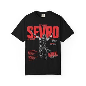 May include: A black short-sleeved t-shirt featuring a red and white graphic print. The design includes the text THE GOBLIN SEVRO AU BARCA, PEERLESS SCARRED, THE RISING, ARES GULD, and a quote about a heart beating like a drum and a reaper.