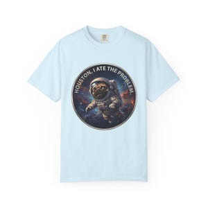 A light blue crewneck t-shirt featuring a circular graphic of a pug in an astronaut suit floating in space with the text HOUSTON, I ATE THE PROBLEM.