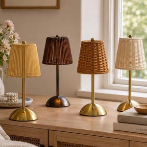 May include: Four table lamps with metallic bases and woven shades. The first lamp has a gold base and light yellow shade, the second a dark bronze base and brown shade, the third a gold base and tan woven shade, and the fourth a gold base and cream shade.