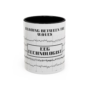 May include: A white ceramic mug with a black interior and rim. The exterior features a black graphic of EEG brain wave lines on a grid background. The text reads READING BETWEEN THE WAVES and EEG TECHNOLOGIST in a bold, black, serif font.