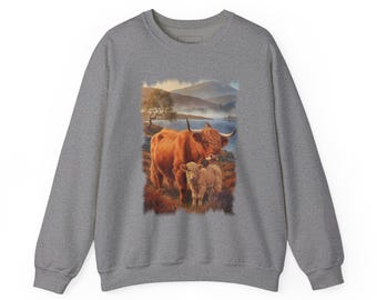 May include: A heather grey crewneck sweatshirt featuring a central graphic print of a ginger Highland cow standing next to a smaller calf in a landscape with a lake, distant mountains, and a small bird perched on the cow's back.