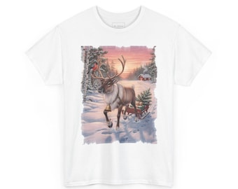 May include: A white t-shirt featuring a graphic print of a reindeer with a bell around its neck, pulling a small sled loaded with gifts through a snowy landscape with pine trees, a small cabin, and a bird perched on an antler.