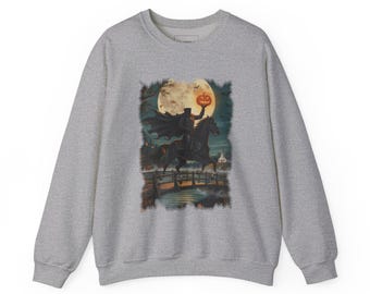 May include: A heather grey crewneck sweatshirt featuring a graphic print of a headless horseman riding a black horse across a bridge. The rider holds a glowing orange jack-o'-lantern against a large full moon and a dark, misty night sky.