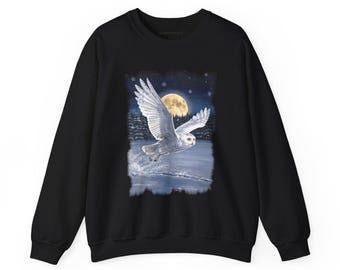 May include: A black long-sleeve sweatshirt featuring a central graphic print of a white snowy owl in flight over a frozen landscape. The scene includes a large yellow full moon, a dark forest silhouette, and falling snowflakes.