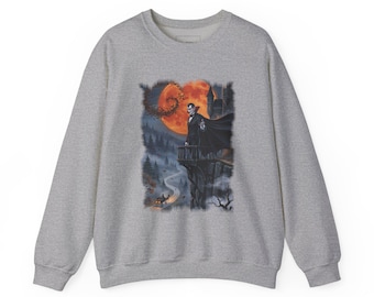 May include: A heather grey crewneck sweatshirt featuring a graphic print of a vampire in a black cape standing on a stone balcony. The scene includes a large orange full moon, a dark castle, a winding road, and a horse-drawn carriage below.