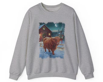May include: A heather grey crewneck sweatshirt featuring a graphic print of a brown Highland cow standing in a snowy landscape at night. The scene includes a red barn with a wreath, a crescent moon, and a fence decorated with string lights.