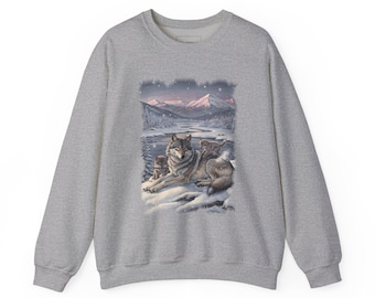 May include: A heather grey crewneck sweatshirt featuring a central graphic print of a wolf and two pups resting in a snowy landscape. The scene includes a winding river, distant mountains under a soft pink sky, and falling snowflakes.
