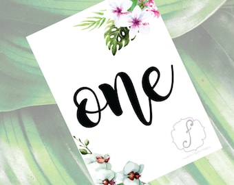 May include: White card with the word "one" written in black cursive script. The card is decorated with pink and white flowers and green leaves. The bottom right corner has a small logo with the letter "F" in a circle.
