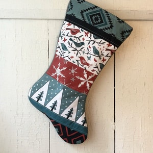 May include: A Christmas stocking with a patchwork design featuring red, white, and blue colors. The stocking has a pattern of birds, snowflakes, and trees.