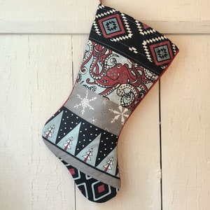May include: A red, gray, black, and blue Christmas stocking with a geometric pattern, an octopus design, and a snowflake pattern.