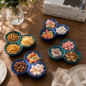 May include: Three clover-shaped ceramic serving dishes in shades of teal and blue, each featuring three rounded compartments. The dishes are filled with various snacks, including colorful candies, marshmallows, nuts, chips, and chocolate-covered treats.
