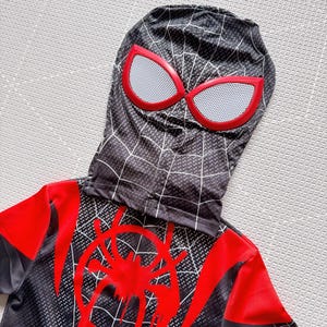 May include: Black and red Spider-Man costume with a hood. The hood features red-rimmed eye shapes with white mesh. The costume has a red spider emblem on the chest and a web pattern design.