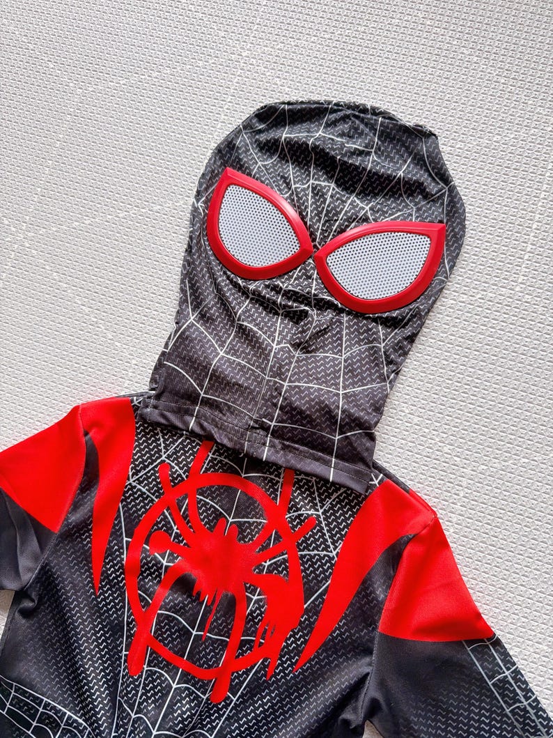 May include: Black and red Spider-Man costume with a hood. The hood features red-rimmed eye shapes with white mesh. The costume has a red spider emblem on the chest and a web pattern design.