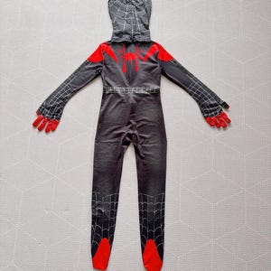 May include: A black and red Spider-Man costume with a hood. The costume features a spider web pattern, red accents on the shoulders, hands, and feet, and a spider emblem on the back. The costume is designed to resemble the character's suit.