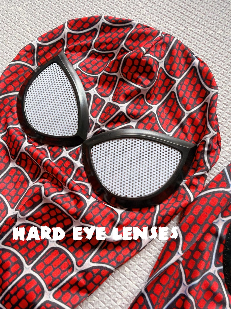 May include: A red and black Spider-Man mask with white eye lenses. The mask features a web pattern design. The text "HARD EYE LENSES" is printed on the mask.