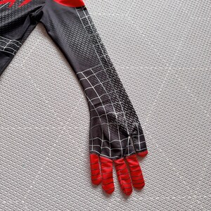 May include: A black and red costume sleeve with a spiderweb design. The sleeve has a red hand with black stripes and a black and gray textured pattern. The costume is likely for cosplay or a superhero theme.
