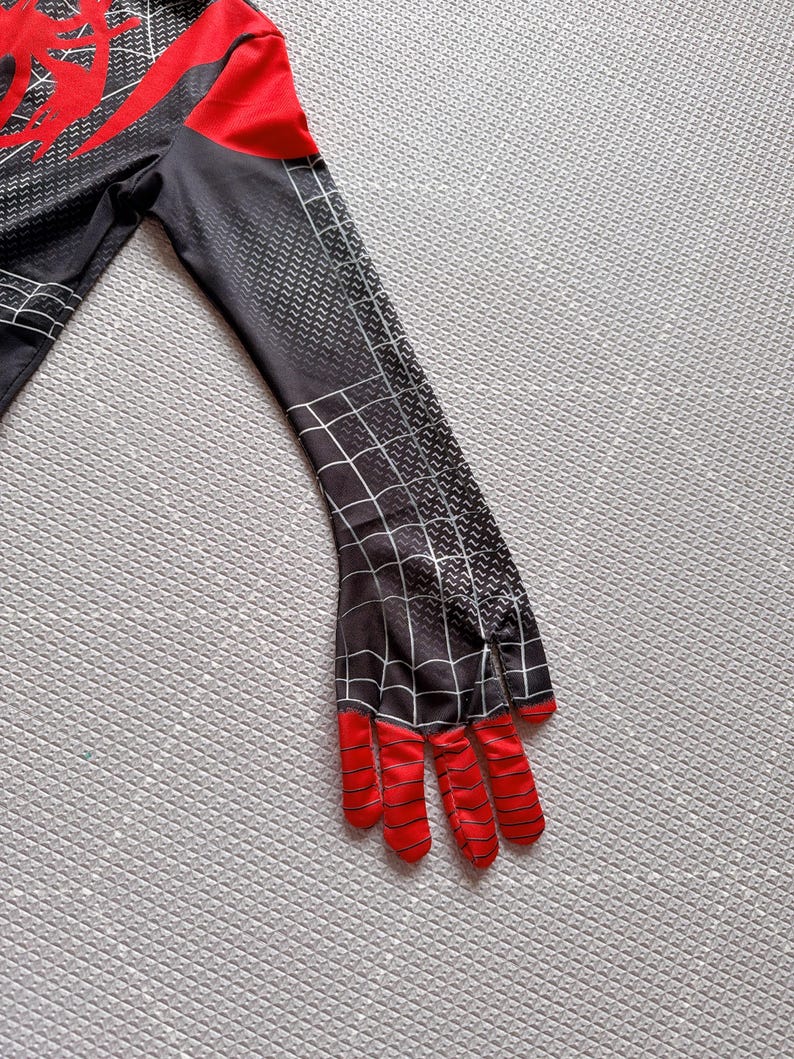 May include: A black and red costume sleeve with a spiderweb design. The sleeve has a red hand with black stripes and a black and gray textured pattern. The costume is likely for cosplay or a superhero theme.