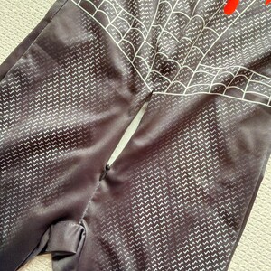 May include: Black jumpsuit with a white web design and red accents. The fabric has a subtle chevron pattern. The jumpsuit appears to be a costume or cosplay outfit.