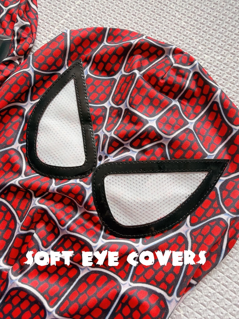 May include: A close-up of a red and black Spider-Man mask with white eye covers. The mask features a web pattern design. The text "SOFT EYE COVERS" is printed in white across the bottom of the image.
