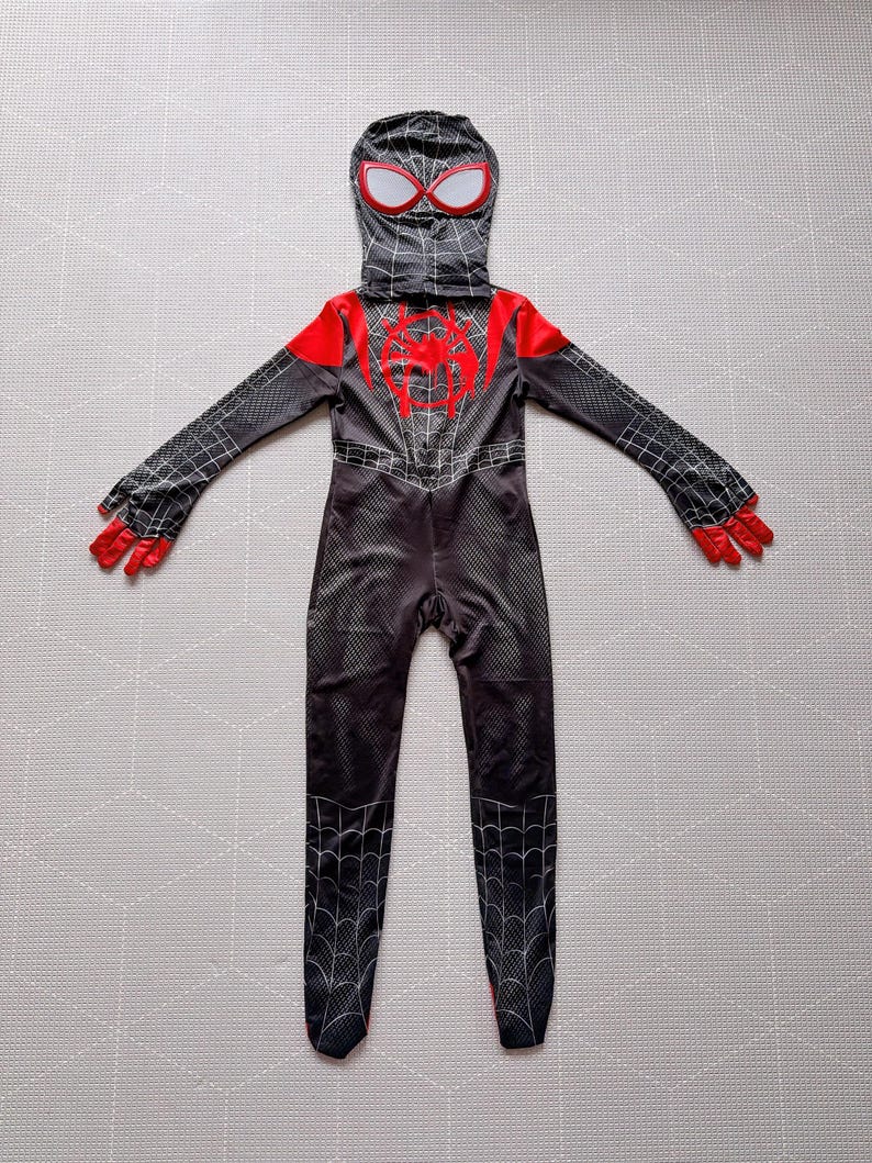 May include: A black and red Spider-Man costume with a hood, gloves, and attached feet. The costume features a spider web pattern and a red spider emblem on the chest. The hood has white-rimmed eye openings.