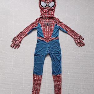 May include: A full-body Spider-Man costume featuring a red and blue color scheme. The costume includes a hood with white eye details, a red spiderweb pattern on the arms and legs, and a spider emblem on the chest. The suit is designed to cover the entire body.