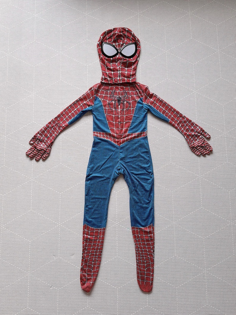 May include: A full-body Spider-Man costume featuring a red and blue color scheme. The costume includes a hood with white eye details, a red spiderweb pattern on the arms and legs, and a spider emblem on the chest. The suit is designed to cover the entire body.
