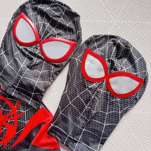 May include: Black and gray Spider-Man costume with white web detailing and red accents. The costume includes a hood with large red-rimmed eye shapes and a matching bodysuit. The design features a web pattern.
